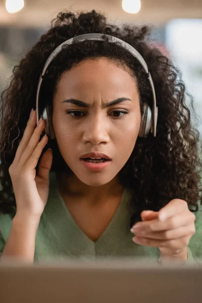 Mujer afroamericana sorprendida escuchando podcast y señalando con el dedo en la cafetería - foto de stock