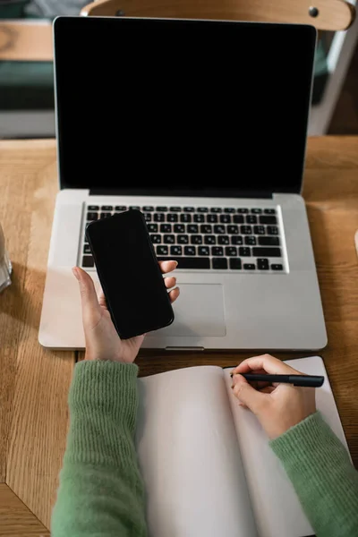 Partial view of african american woman holding smartphone with blank screen near laptop and notebook — Stock Photo