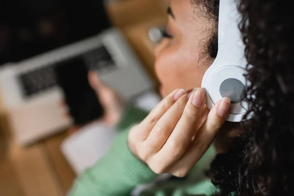 Mujer afroamericana escuchando podcast y tocando auriculares - foto de stock