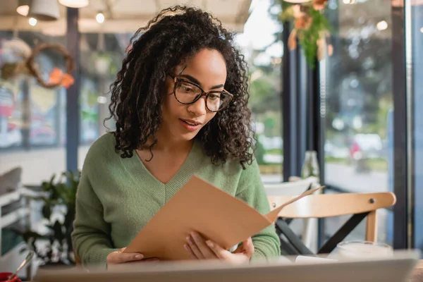 Ricci donna africana americana in bicchieri che tengono il menu nel caffè — Foto stock