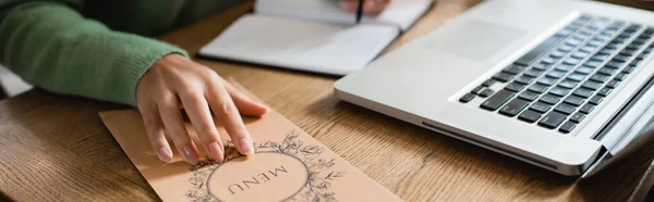 Ausgeschnittene Ansicht einer afrikanisch-amerikanischen Frau anrührende Broschüre mit Menü-Schriftzug auf Tisch, Banner — Stockfoto