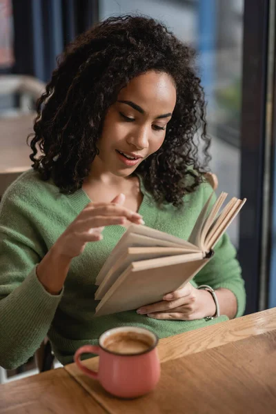 Mujer afroamericana hojeando páginas de libro en la cafetería - foto de stock