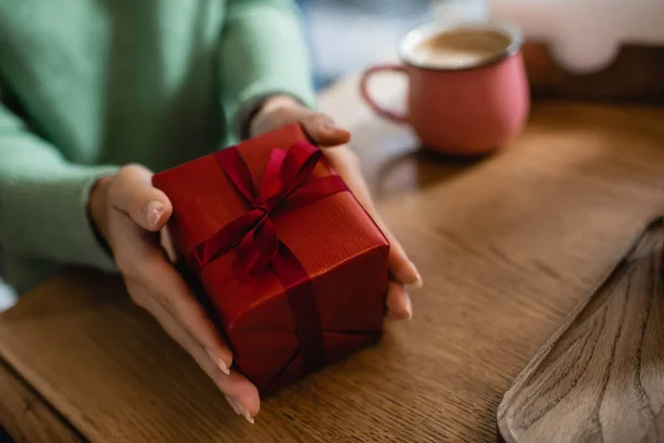 Cropped view of african american woman holding wrapped christmas gift in cafe — Stock Photo