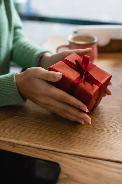 Partial view of african american woman holding wrapped christmas gift in cafe — Stock Photo