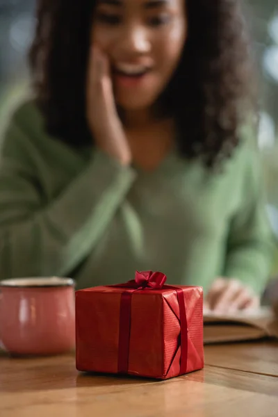 Scatola regalo di Natale rosso vicino stupito donna africana americana su sfondo sfocato — Foto stock