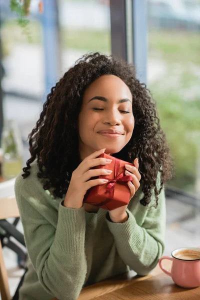 Pleased african american woman with closed eyes holding christmas gift — Stock Photo
