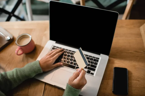 Partial view of african american woman holding credit card near laptop with blank screen — Stock Photo