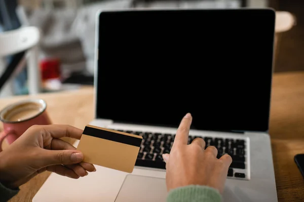 Vista recortada de la joven afroamericana que sostiene la tarjeta de crédito cerca de la computadora portátil con pantalla en blanco - foto de stock