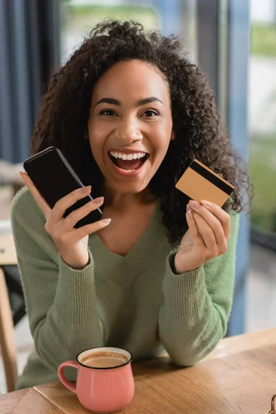 Excited african american woman holding smartphone and credit card — Stock Photo