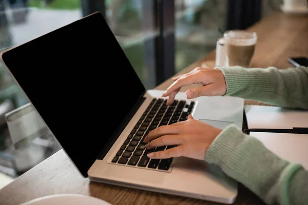 Vista recortada de la mujer afroamericana escribiendo en el ordenador portátil con pantalla en blanco en la mesa - foto de stock