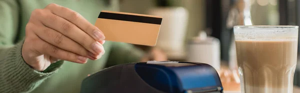 Verre de latte près de carte de crédit en main de femme afro-américaine payant sur fond flou, bannière — Photo de stock