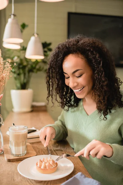 Fröhliche afrikanisch-amerikanische Frau hält Besteck in der Nähe von Torte auf Teller — Stockfoto