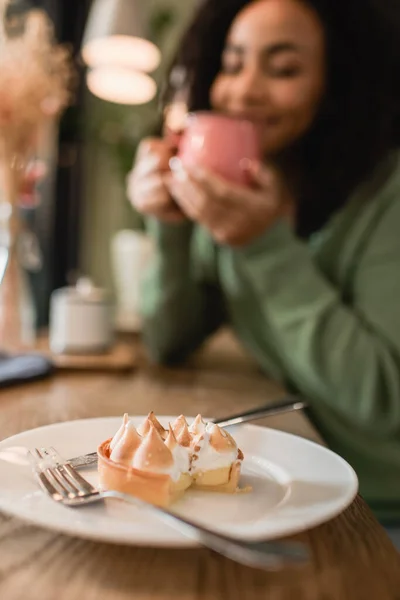 Sabrosa tarta en el plato cerca de la mujer afroamericana sobre fondo borroso - foto de stock