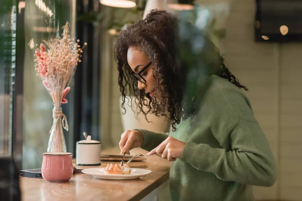 African american woman in eyeglasses holding cutlery near tart on plate — Stock Photo
