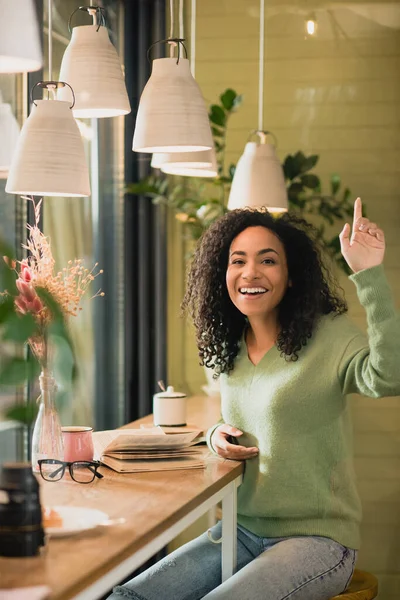 Alegre mujer afroamericana gesto mientras pide factura en la cafetería - foto de stock