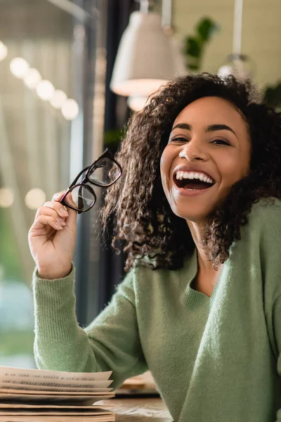 Afro-américaine femme tenant des lunettes et riant dans le café — Photo de stock