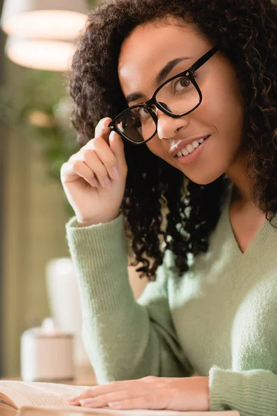 Happy african american woman adjusting eyeglasses and looking at camera — Stock Photo