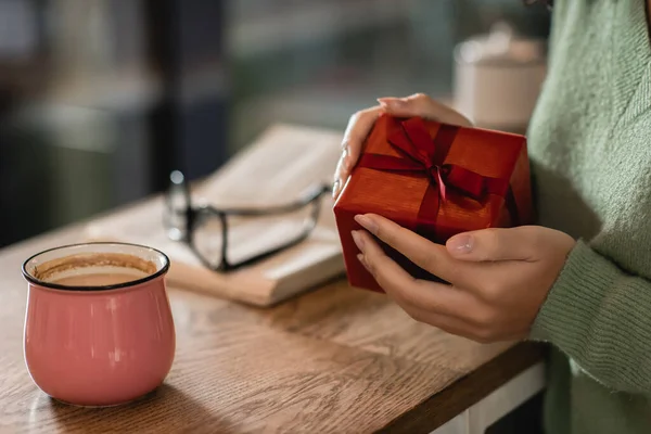 Cropped view of african american woman holding wrapped christmas present in cafe — Stock Photo