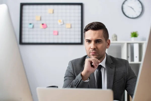 Serious trader looking at monitors in office, blurred foreground — Stock Photo