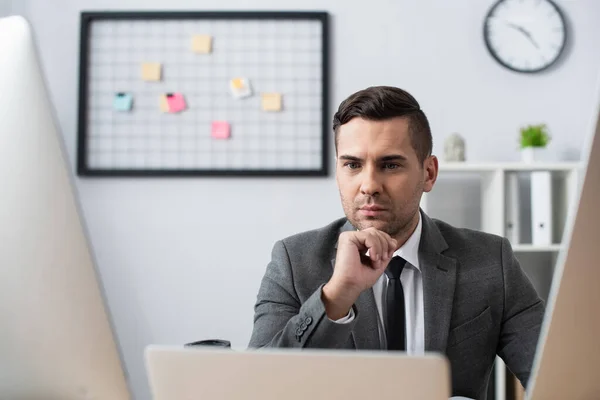 Seriöser Händler blickt auf Monitore im Büro, verschwommener Vordergrund — Stockfoto