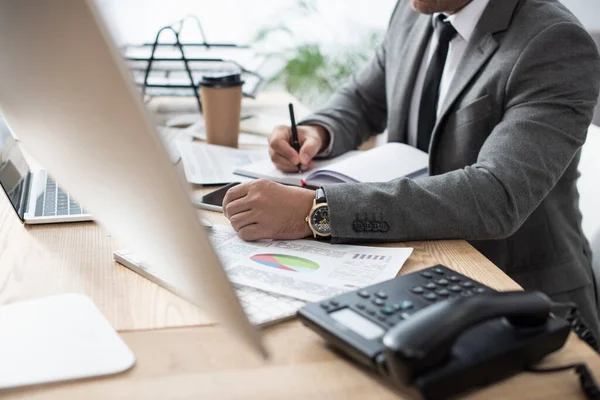 Partial view of trader writing in notebook near landline phone on blurred foreground — Stock Photo