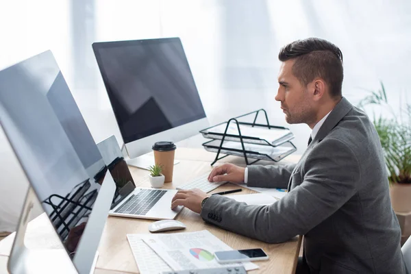 Vista laterale del commerciante sul posto di lavoro vicino laptop e monitor con schermo vuoto — Foto stock