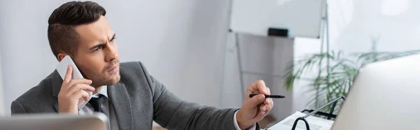 Hombre de negocios serio hablando en el teléfono inteligente y apuntando con la pluma en primer plano borrosa, bandera - foto de stock