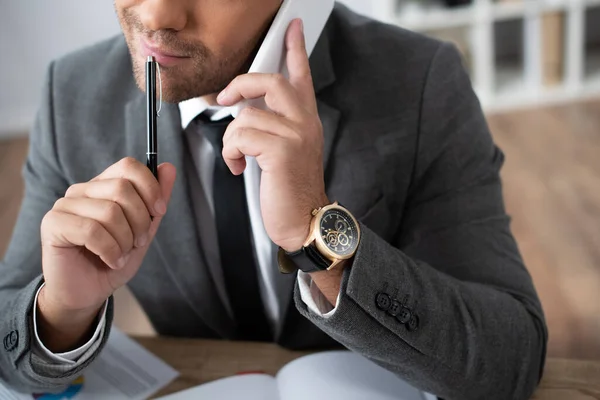 Recortado vista de empresario celebración de pluma mientras habla en el teléfono inteligente - foto de stock