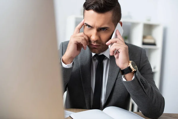 Homem de negócios pensativo falando no smartphone no escritório, foreground borrado — Fotografia de Stock