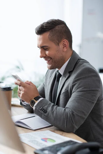 Smiling trader messaging on smartphone at workplace on blurred foreground — Stock Photo