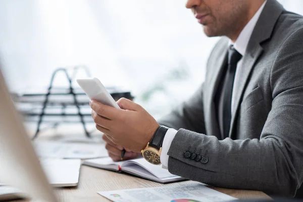 Vista recortada de la mensajería de hombre de negocios en el teléfono inteligente en el lugar de trabajo en primer plano borrosa - foto de stock