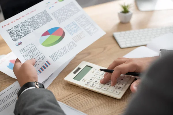 Ausgeschnittene Ansicht des Händlers, der mit Taschenrechner und Infografik im Büro arbeitet, verschwommener Vordergrund — Stockfoto