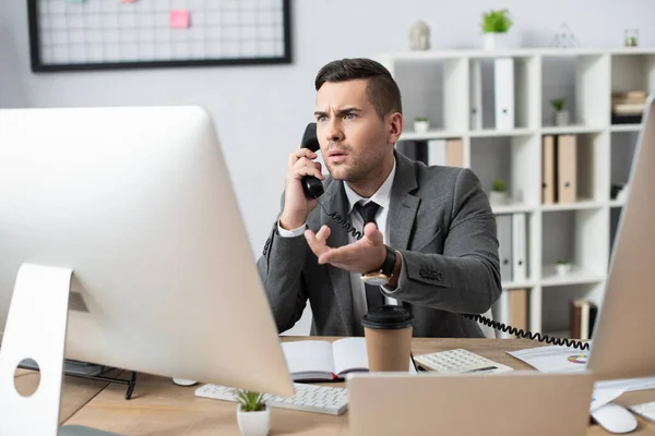 Geschockter Händler zeigt bei Telefongespräch mit der Hand auf Computermonitor — Stockfoto