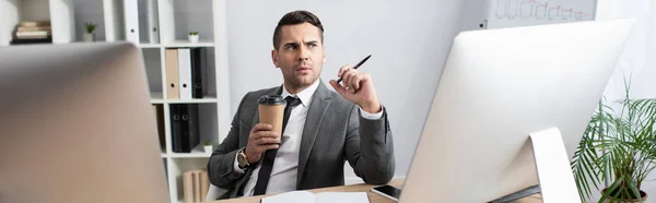 Nachdenklicher Händler mit Coffee to go und Stift in der Nähe von Computermonitoren, Banner — Stockfoto