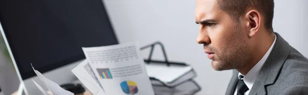 Comerciante reflexivo mirando infografías cerca de monitor en la oficina, bandera - foto de stock