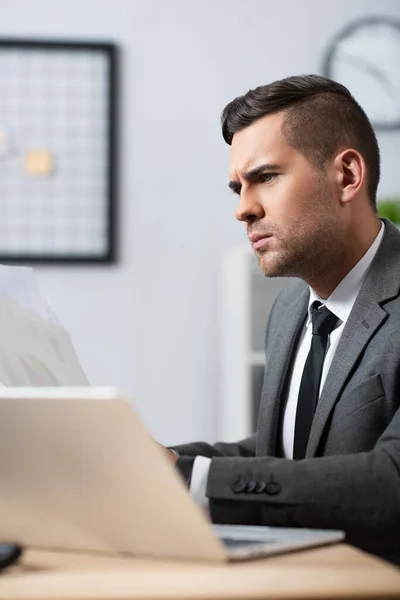 Uomo d'affari premuroso che lavora in ufficio vicino al computer portatile, primo piano sfocato — Foto stock