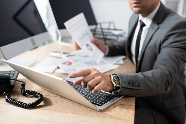 Vista recortada del comerciante apuntando con el dedo a la computadora portátil, fondo borroso - foto de stock