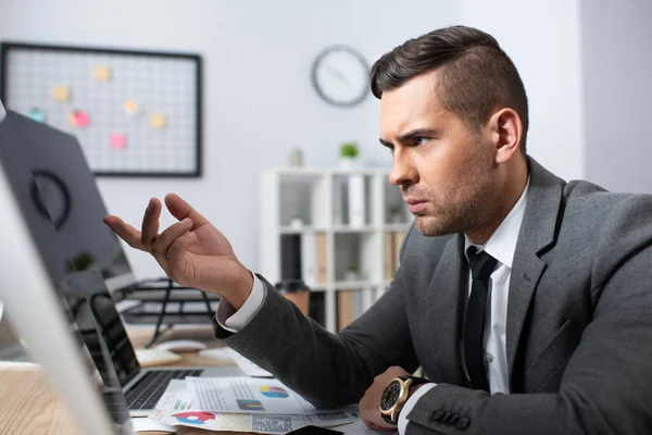 Empresário sério apontando com o dedo para o monitor em primeiro plano desfocado — Fotografia de Stock