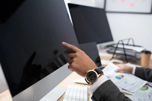 Vista recortada del comerciante en reloj de pulsera apuntando al monitor con pantalla en blanco - foto de stock