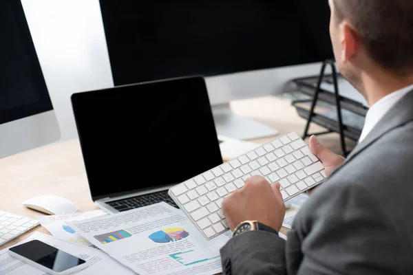 Ausgeschnittene Ansicht der Eingabe des Händlers auf der Tastatur in der Nähe von Laptop und Monitoren mit leerem Bildschirm — Stockfoto