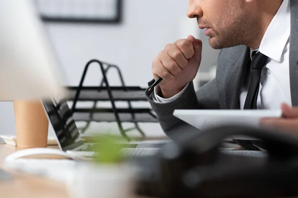 Ausgeschnittene Ansicht eines konzentrierten Händlers mit Stift am Arbeitsplatz, verschwommener Vordergrund — Stockfoto