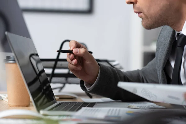 Vista ritagliata del commerciante che punta con la penna al computer portatile, primo piano sfocato — Foto stock