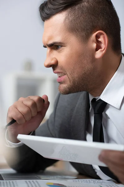 Worried trader holding pen in office, blurred foreground — Stock Photo