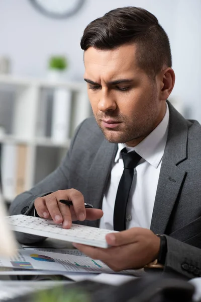 Händler hält Stift beim Tippen auf der Tastatur im Büro, verschwommener Vordergrund — Stockfoto