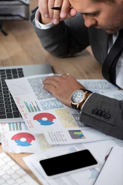 Trader working with infographics near laptop and smartphone with blank screen, blurred foreground — Stock Photo