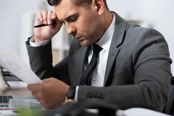 Commerçant épuisé tenant stylo et papier tout en étant assis sur le lieu de travail avec les yeux fermés, au premier plan flou — Photo de stock