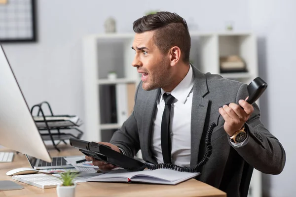 Comerciante chocado segurando auscultador enquanto olha para o monitor do computador, foreground borrado — Fotografia de Stock