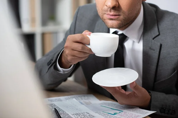 Cropped view of trader holding coffee cup at workplace, blurred foreground — Stock Photo