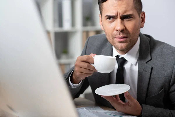 Empresário pensativo segurando xícara de café no local de trabalho, foreground turvo — Fotografia de Stock