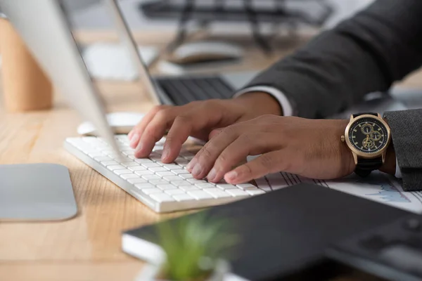 Ausgeschnittene Ansicht des Händlers in Armbanduhr Tippen auf der Tastatur auf verschwommenem Vordergrund — Stockfoto